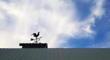 hühnerwindmühle auf dach mit blauem himmel und wolkenhintergrund mit kopienraum. Objekt zum Sagen von Windrichtung und -stärke. Silhouette der Tierstatue. foto