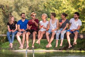 freunde, die wassermelone genießen, während sie auf der holzbrücke sitzen foto