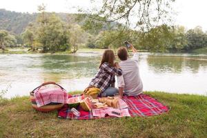 Paar, das ein Selfie mit dem Handy macht, während es die Picknickzeit genießt foto