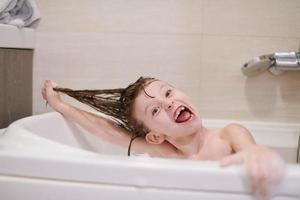 kleines Mädchen im Bad, das mit Seifenschaum spielt foto