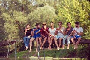 freunde, die wassermelone genießen, während sie auf der holzbrücke sitzen foto