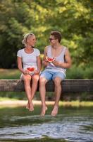 Paar genießt Wassermelone, während es auf der Holzbrücke sitzt foto