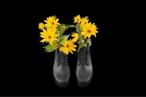 Schwarze Damen-Plateaustiefel mit Strauß gelber Topinambur-Blumen, schwarzer Hintergrund foto