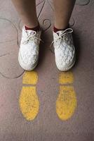 Füße und Pfeile auf der Straße. gelbes gerades Pfeilzeichen und weiße Schuhe. Konzept der geraden Richtung. Reisekonzept foto