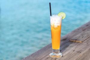 sommerferienkonzept, fruchtcocktailglas. willkommensgetränk orangensaftpunsch auf holztisch fast am meer. foto