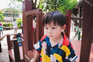 asiatischer junge spielt auf dem spielplatz im freien. im Sommer oder Frühling. Das Kind fühlte sich heiß und verschwitzt im Gesicht an. kümmert sich bei heißem wetter um die gesundheit des jungen kindes. Baby 2-3 Jahre alt. Kinder tragen ein buntes Kleid foto