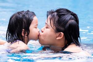 Porträt von Mutter und Tochter küssen sich. bild einer asiatischen familie, die liebe und bindung zeigt. Frauen und kleine Mädchen spielen im Wasserbecken des Resorts. in der Sommerzeit. Kinder 4-5 Jahre alt. foto