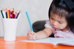 eine 4-5 jährige asiatin arbeitet hart an ihrer aufgabe. Kinder sitzen und schreiben Hausaufgaben. Kinder lernen zu Hause. am Schreibtisch sitzen und lernen. foto