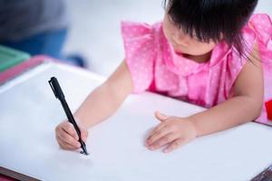 selektiver fokus kinderhand, die magischen stift hält. asiatisches süßes mädchen, das kunst auf weißem papier macht. glückliches kind, das handwerk homeschool lernt. Schüler, der Hausaufgaben macht. Hobbyzeit Kindergarten. Frau im Alter von 4 Jahren. foto