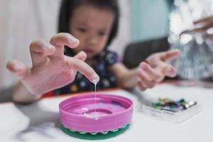 selektiver Fokus. Die Hand des kleinen Mädchens berührt den weißen Kleber in der rosa Plastikkappe. Kinder machen Kunstwerke mit Paste und Stock. Konzept der Meditation und des Lernens. Kind im Alter von 4-5 Jahren. foto