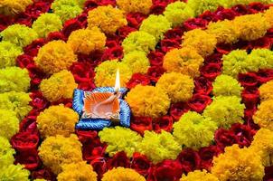 dekorative ringelblumen- und rosenblüten-rangoli für diwali-fest mit lehm-diya-lampe, die mit flamme beleuchtet ist. foto