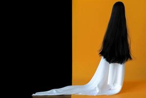 langhaariger weiblicher geist mit weißem blattkostüm mit schwarzem und orangefarbenem hintergrund. minimales gruseliges halloween-konzept. foto