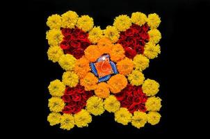 dekorative ringelblumen- und rosenblumen rangoli für das diwali-fest mit lehm-diya-lampe, die mit unscharfer fokusflamme auf schwarzem hintergrund beleuchtet wird. foto