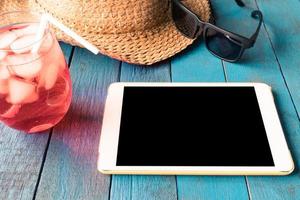 tablet mit hut, sonnenbrille und rotem cocktail auf blau lackiertem holzplankenhintergrund. foto