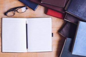 leeres notizbuch mit bleistift, brille und büchern auf holztisch. foto