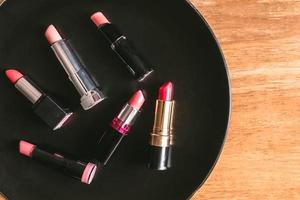 Draufsicht auf bunte Lippenstifte auf der schwarzen Platte über dem Holztisch. Make-up und Schönheitskonzept foto