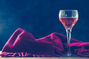 Glas Wein mit rotem Schal auf dem Tisch, schwarzer Hintergrund, freier Platz für Text, Vintage-Ton foto