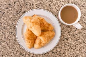 frühstück mit tasse kaffee, croissant auf dem tisch. foto