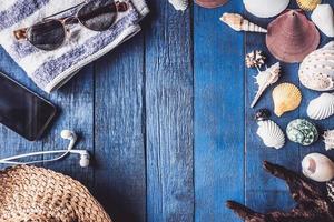 Draufsicht auf Zubehör für Sommerreise mit Muscheln auf blau lackiertem Holzbretthintergrund. foto