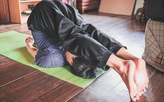 junger asiatischer mann, der yoga in einem holzzimmer praktiziert, das in pose pflugpose auf einer grünen yogamatte in einem holzhaus sitzt. gesundes lebenskonzept foto