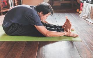 junger asiatischer mann, der yoga praktiziert, sitzt in sitzender vorwärtsbeugeübung, paschimottanasana-pose auf grüner matte yoga im holzhaus. gesundes Leben foto