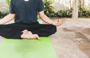 junger asiatischer mann, der yoga, atmung, meditation, adha-übung, padmasana, halbe lotoshaltung mit schlammhaltung auf der grünen yogamatte praktiziert. übung im garten.gesundes lebenskonzept foto