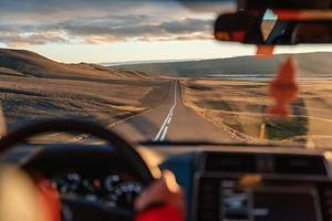 Mann, der im Sonnenuntergang ein Auto durch die Wildnis auf Asphaltstraße fährt foto