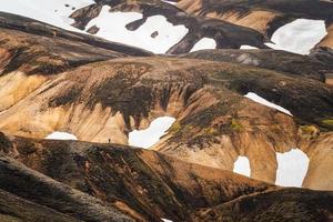 landschaftlich reizvoller vulkanischer berg mit schneebedeckten und wanderern, die auf dem grat im fjallabak-naturschutzgebiet im isländischen hochland bei landmannalaugar, island, spazieren gehen foto