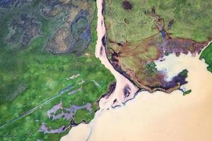 idyllisches mineralisches geologisches gelbes meer, das im sommer in island zum ozean und durch grüne feuchtgebiete fließt foto