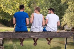 Männer genießen Wassermelone, während sie auf der Holzbrücke sitzen foto