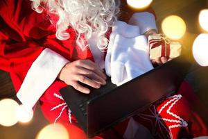 weihnachtsmann mit einem laptop und einem geschenk in der hand. Bestellen Sie Geschenke für Weihnachten und Silvester über den Online-Shop. Buchung der Dienste eines Animateurs für die Feiertage. foto