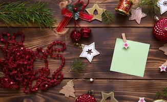 weihnachtsflache lage aus roten luftballons und holzsternen und wäscheklammern auf dunklem hintergrund mit einem quadratischen blatt für notizen in der mitte. neujahrsrahmen, platz für text. Weihnachtsspielzeug, Perlen, Tannenzweige foto