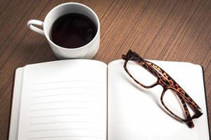 Brille auf leerem Notizbuch und Kaffee über Holztisch