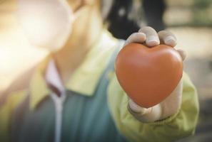 eine hand, die rotes herz hält. sie ist die linke oder rechte hand, die es auf grünem hintergrund hält. herzgesundheit, glückliche freiwillige wohltätigkeit, das foto zeigt das prinzip der fürsorglichkeit und der guten gesundheit.