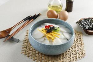 koreanische scheibenkuchensuppe oder tteokguk auf blauer schüssel. Topping mit Ei, Chili, Seetang und Frühlingszwiebeln foto