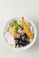 Udon mit Meeresfrüchtebrühe, knusprigem Tempura, Frühlingszwiebeln und Narutomaki-Topping. foto