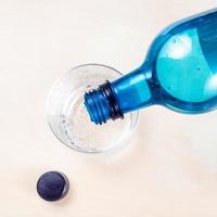 Wasser aus blauer Plastikflasche in Glas gießen foto