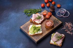 Frische, leckere Sandwiches mit Schinken, Butter, Avocado und Sesamsamen auf einem Holzschneidebrett