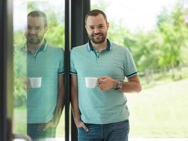 junger Mann trinkt Morgenkaffee am Fenster foto