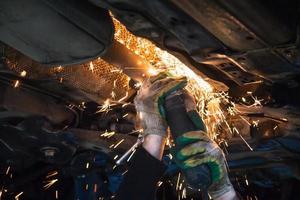 Mechaniker schneidet alten Schalldämpfer am Auto mit Winkelschleifer foto