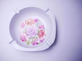 weißer Zigarettenaschenbecher mit Blumenmotiv in der Mitte. Aschenbecher isoliert auf weißem Hintergrund. Aschenbecher werden oft von Rauchern verwendet, um Zigarettenasche oder Zigarettenkippen zu entsorgen foto