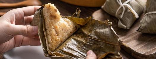 essen zongzi - drachenbootfestival reisknödel junge asiatische frau, die chinesisches traditionelles essen auf holztisch zu hause feier isst, nahaufnahme foto