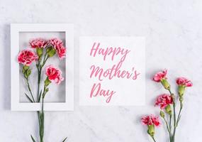 Happy Mother's Day Hintergrunddesignkonzept mit Grußworten, schöner rosafarbener, roter Nelkenblumenstrauß auf Marmortisch, Draufsicht, flache Lage, Kopierraum. foto