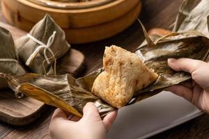 Dragon Boat Festival Essen - Reisknödel Zongzi, junge asiatische Frau, die chinesisches traditionelles Essen auf Holztisch zu Hause isst, Feier, Nahaufnahme foto