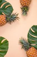 Schöne Ananas auf tropischen Palmen-Monstera-Blättern isoliert auf hellem pastellorangefarbenem Hintergrund, Draufsicht, flache Lage, Overhead über Sommerfrüchten. foto