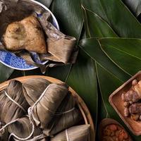 reisknödel, zongzi - traditionelles chinesisches essen auf grünem blatthintergrund des drachenbootfestivals, duanwu-festival, draufsicht, flaches lagdesignkonzept. foto