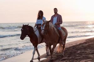 Ein liebevolles Paar in Sommerkleidung, das bei Sonnenuntergang an einem Sandstrand reitet. Meer und Sonnenuntergang im Hintergrund. selektiver Fokus foto