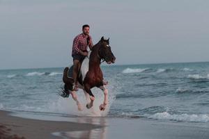 ein moderner mann in sommerkleidung genießt es, bei sonnenuntergang an einem schönen sandstrand zu reiten. selektiver Fokus foto