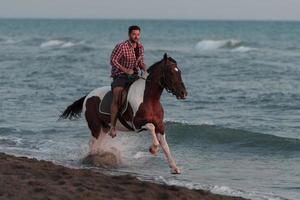 ein moderner mann in sommerkleidung genießt es, bei sonnenuntergang an einem schönen sandstrand zu reiten. selektiver Fokus foto