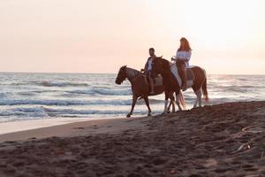 Ein liebevolles Paar in Sommerkleidung, das bei Sonnenuntergang an einem Sandstrand reitet. Meer und Sonnenuntergang im Hintergrund. selektiver Fokus foto